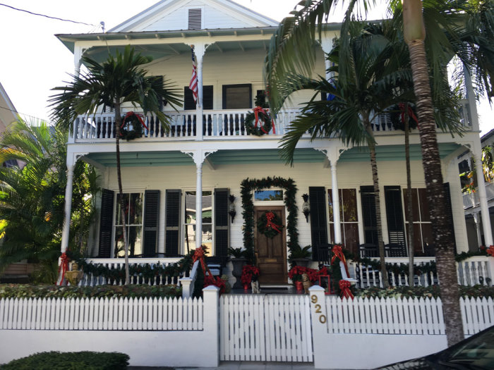 Tvåvåningshus i Key West med vit picketstaket och juldekorationer, inklusive kransar och röda rosetter.