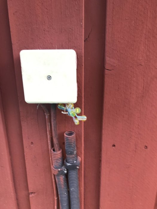 Utomhuskåpa på röd vägg med nedglidet svart plaströr som exponerar färgglada eltrådar och anslutningar.