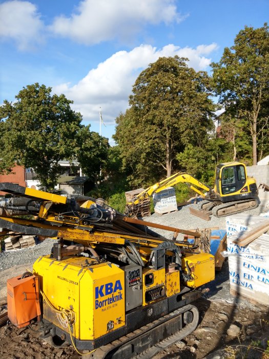 Borrigg för bergvärme på byggarbetsplats med grävmaskiner och byggmaterial i bakgrunden.