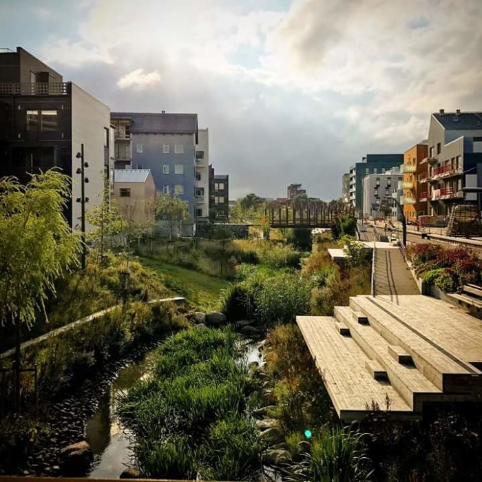 Vy över Vallastaden med moderna byggnader, en grön park och en gångväg nära vatten.