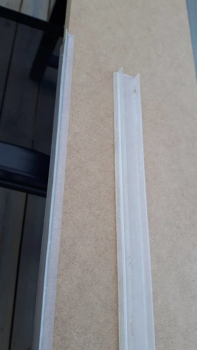 Två vita plastlister på en spånskiva, avsedda för att skydda mot vattenintrång i kök.
