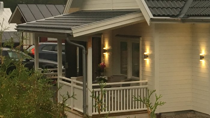 Invändig hörna av ett nybyggt hus med veranda, vita väggar, och belysning på kvällstid.