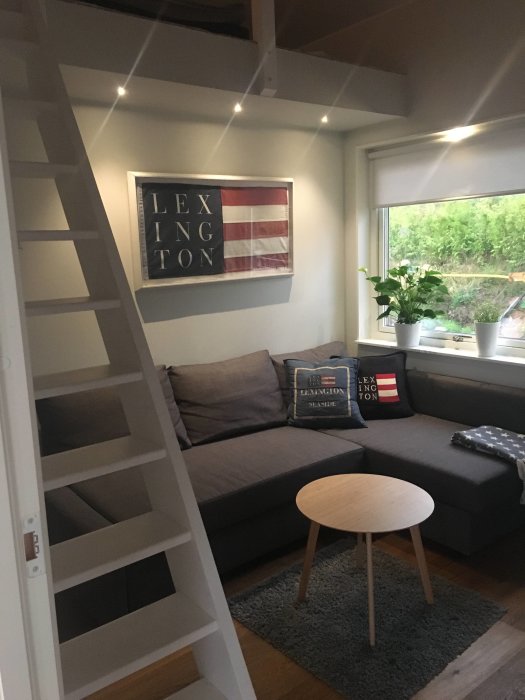 Inredning av vardagsrum med soffa, kuddar, amerikansk flagga-tavla och vit trappa.