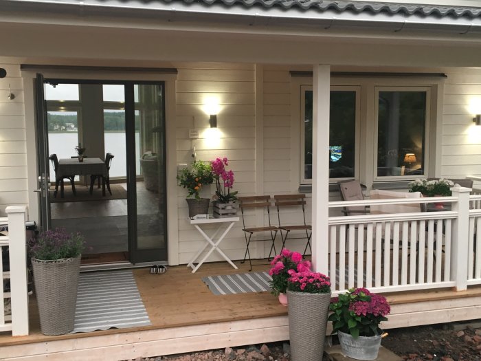 Vitmålat trähus med öppen veranda, möbler och blomsterarrangemang som visar den hemtrevliga exteriören.
