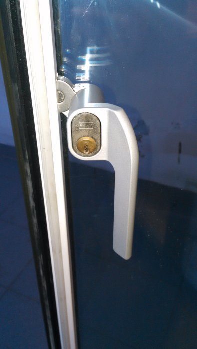 Oval låscylinder i dörr med handtag och låsbricka, synlig cylinderskruv.