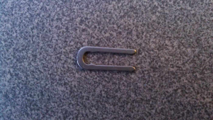 Metal låsbricka för låscylinder med två guldtonade tips mot grå bakgrund.