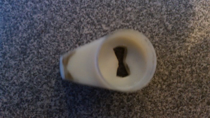 Oval låsbricka för låscylinder med synligt spår för cylinderskruv på grå bakgrund.