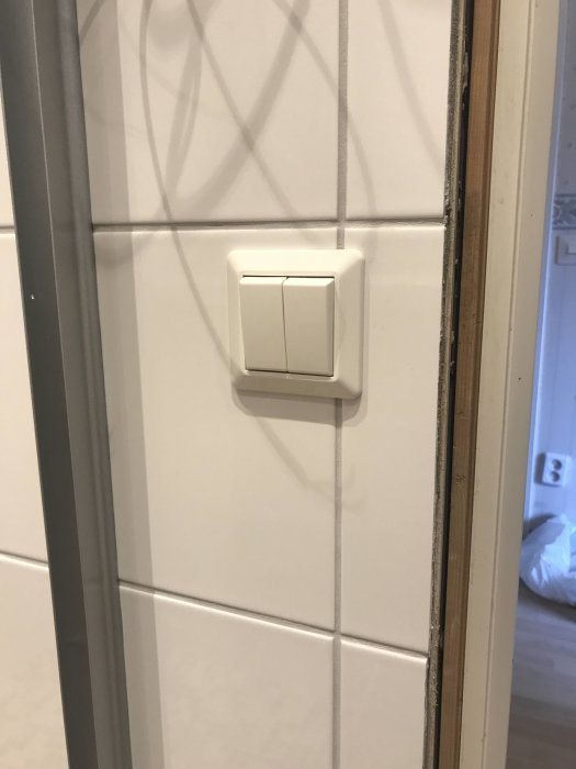 Strömbrytare och manöverpanel installerade på vit kaklad vägg bredvid en duschdörr i ett renoverat badrum.