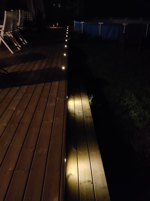 Installerade Cosa 45 lampor längs träaltanens kant lyser upp i mörkret med poolen i bakgrunden.