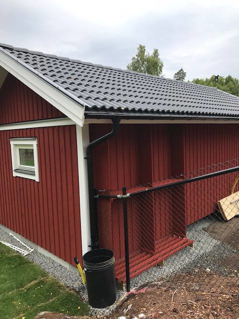 Nymålat rött hundhus med staket och takutsprånget på ett nybyggt hus, omgiven av grus och stenar.