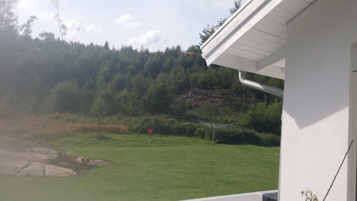 Vy över en gräsmatta med en lekställning mot ett skogsbeklätt berg där byggnation ska ske.