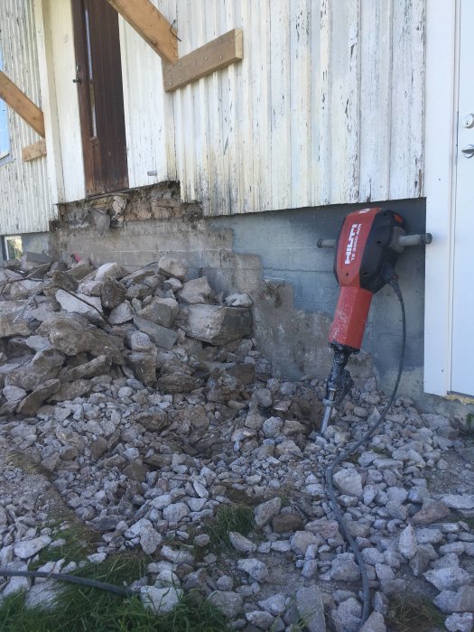 Rivningsarbete vid husgrund med en hög av krossad betong och en eldriven jackhammare.