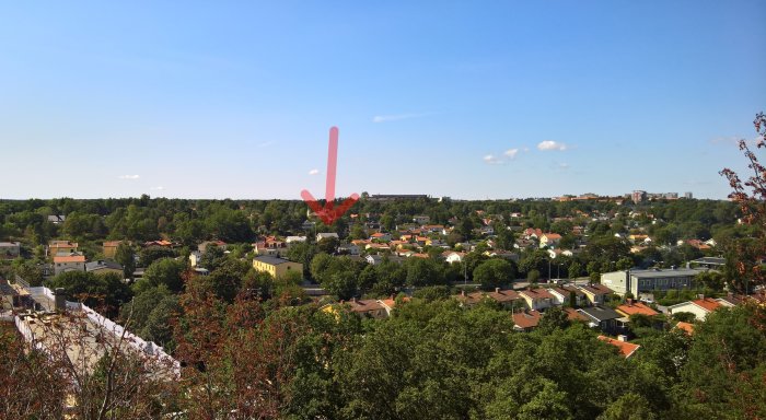 Vy över förortsområde med röd pil som pekar mot ett hus, träd i förgrunden och klarblå himmel.