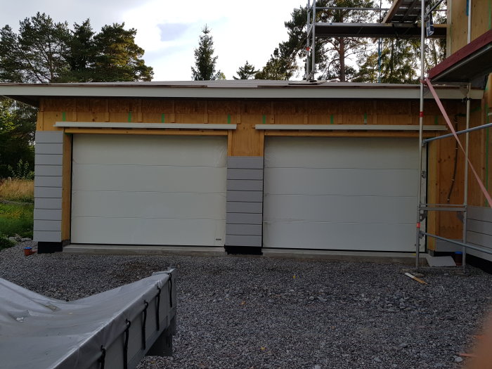 Nyinstallerade garageportar med en Hörmann-motor synlig på ena porten, omgiven av grus och arbetsmaterial.