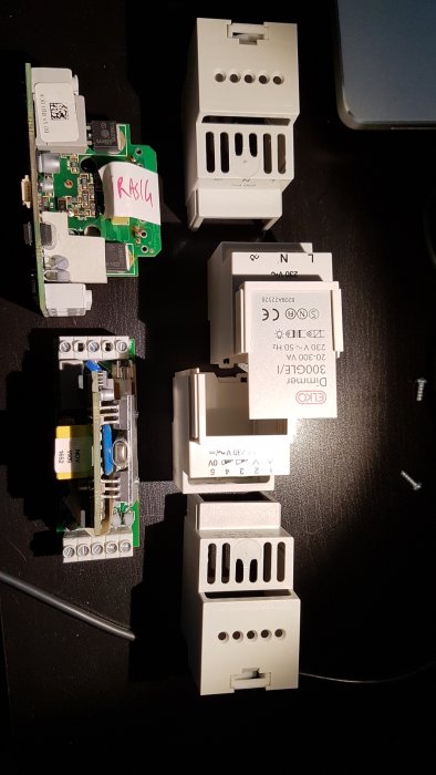 Två isärtagna elektroniska dimmerenheter och deras vit plastkapslingar för DIN-skenmontering.