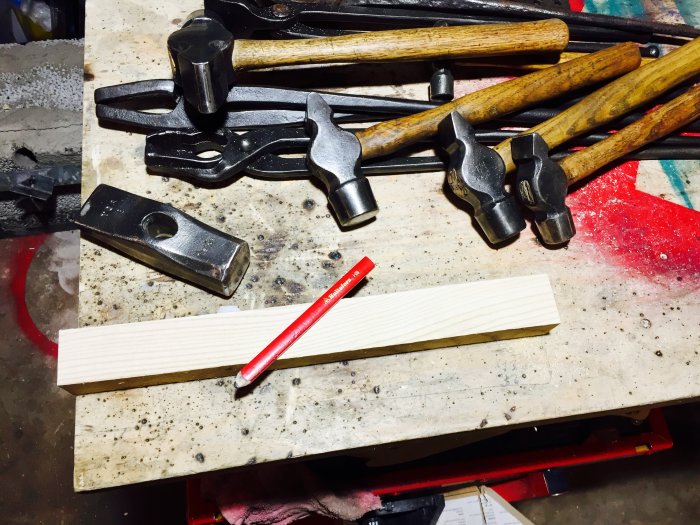 Renoverade hammare och smidesverktyg på ett arbetsbord med nya skaft i askträ och röd blyertspenna.