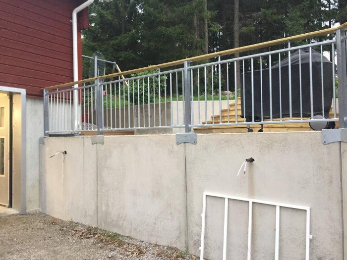 Nybyggt staket längs med betongvägg vid garage, med material och verktyg synliga.