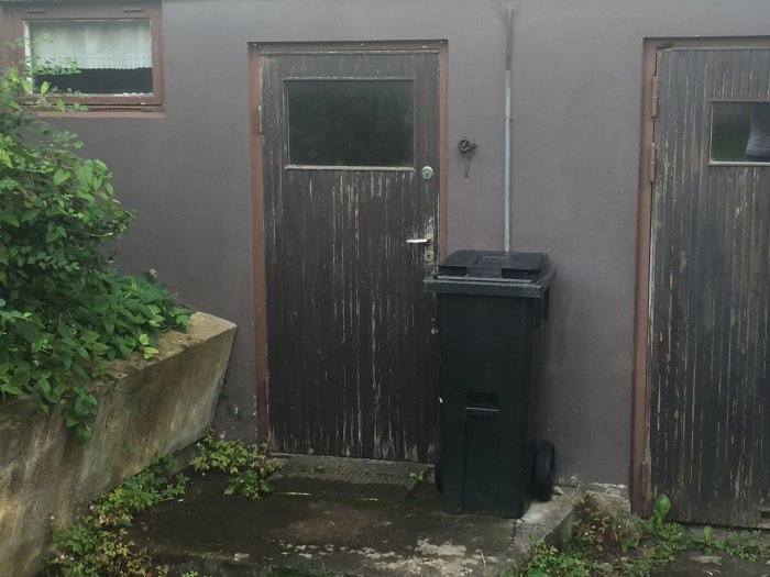 Söndervittrad stödmur och två garageportar i trä med tecken på slitage vid ett 50-talshus.