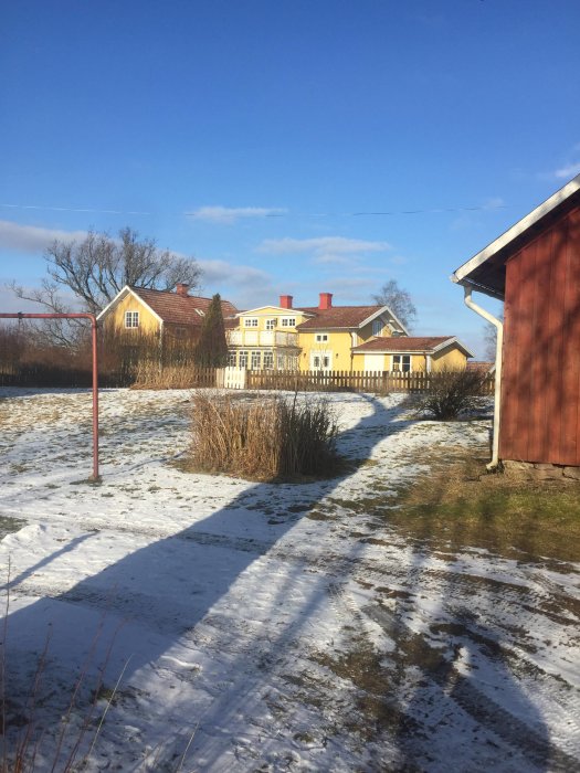 Gult 70-tals hus med omålade räcken på glasverandan, snö och grått gräs i förgrunden.