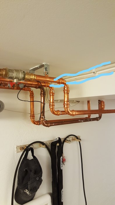 Kopparledningar med T-koppling och avslutad sektion märkt med blå linje under tak i ett rum.