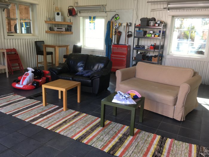 Garage inrett som vardagsrum med soffa, stolar och leksaksbil på ett färgglatt mattgolv.