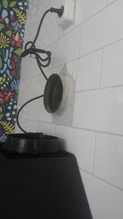 Köksfläkt framför kaklad vägg med synlig öppning för utblåsrör och sladdar anslutna till uttag.