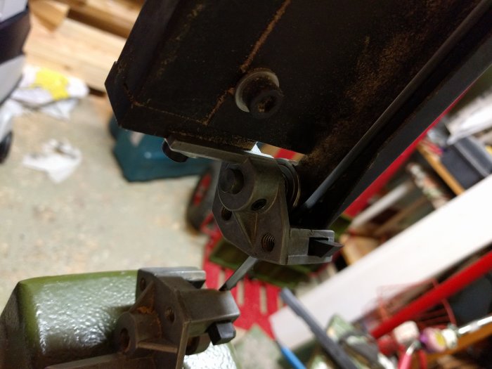 Närbild av bandsågsblad och dess styrningssystem i ett garage.
