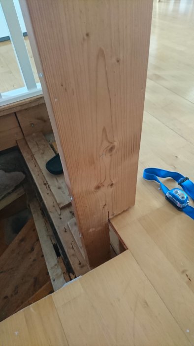 En ny träpelare på ett golv bredvid ett uppsågat hål där avloppsrör syns, med måttband.
