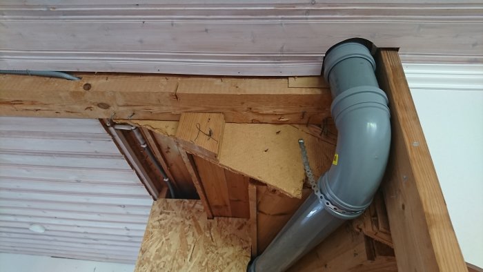 Renoveringsprojekt med gråa avloppsrör nära träbjälkar och oskyddade kablar i taket.