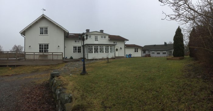 Vit villa med veranda och grön gräsmatta under grå himmel.