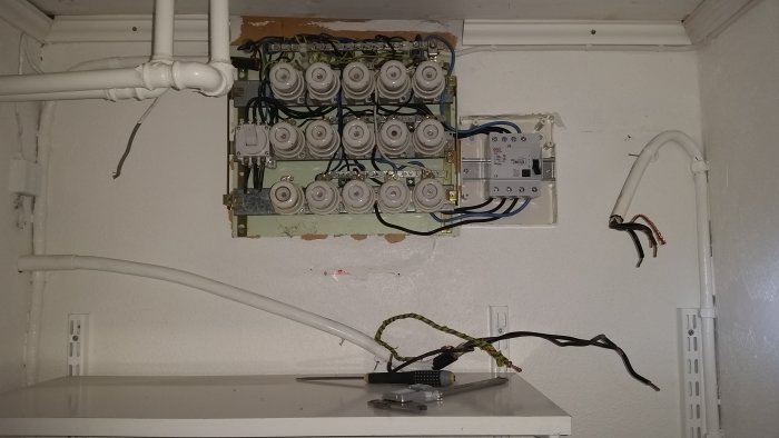 Gammal elcentral med uppkopplade säkringar och avlägsnade ledningar, verktyg på hylla nedanför.