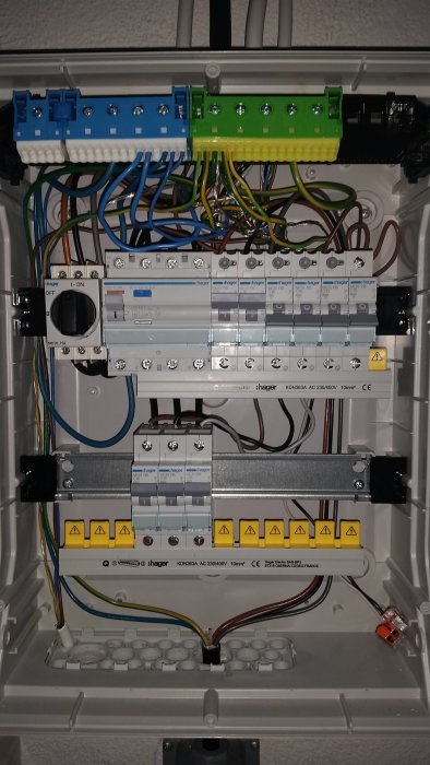 Elektrisk fördelningscentral med ledningar, automatsäkringar och en märkt omkopplare.