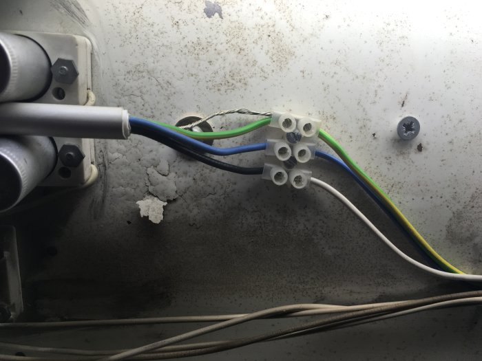 Elektriska kablar kopplade till en plint inuti en armatur, jord och skyddskabel till samma punkt.