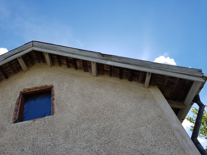 Gavel på hus med synliga takbjälkar och putsad fasad under blå himmel.