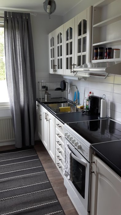 Nästan färdigt kök med vita skåp, svart bänkskiva och modern spis, väntar på slutgiltiga detaljer.