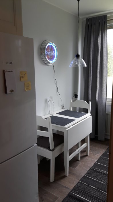 Renoverat kök med vit matplats, kylskåp och Coca-Cola neonskylt på väggen.