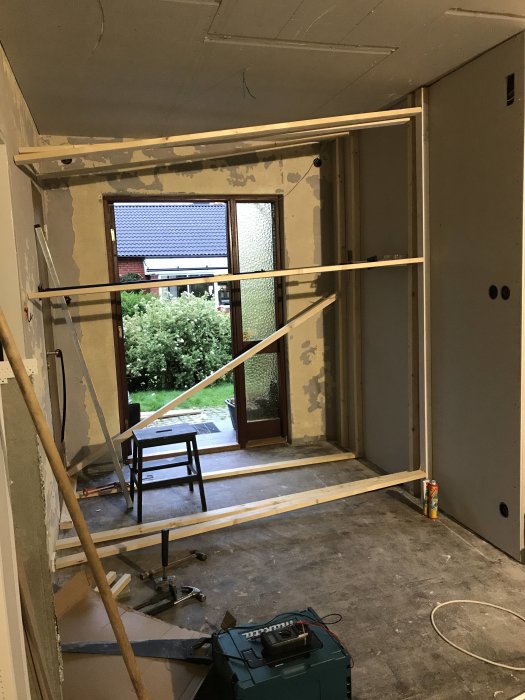 Renoveringsarbete med gipsvägg, träreglar och verktyg i ett rum under konstruktion.