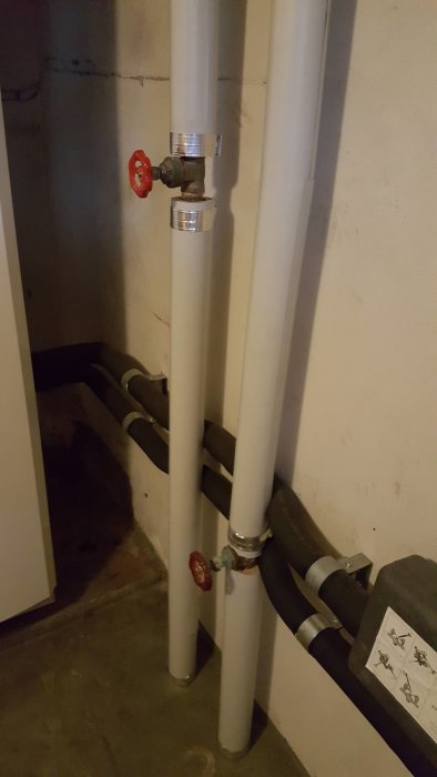 Vattenrör och ventiler i en källare med tecken på möjlig läckage.