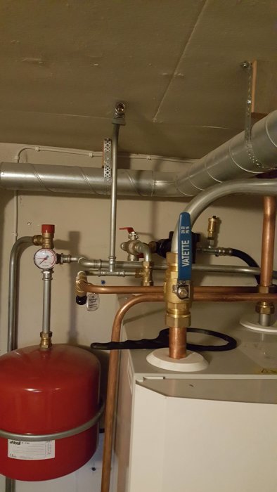 Värmepumpsinstallation med rör, manometer och expansionskärl i källare.