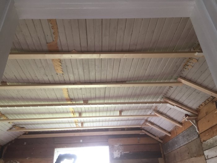 Renoveringsprojekt av ett sänkt tak i rum, med vita takpannlar och exponerade träbjälkar.