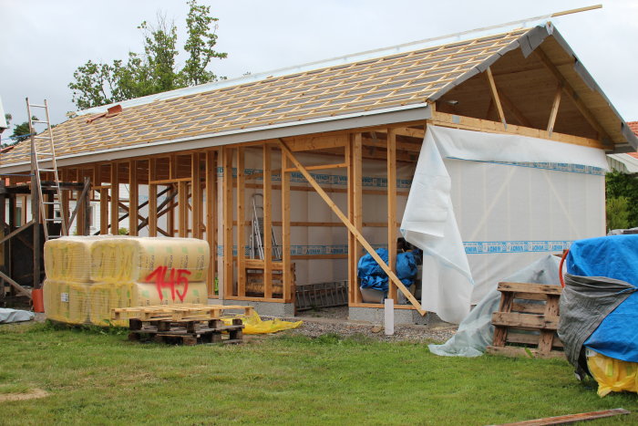 Hus under konstruktion med trästomme och oisolerad takstol, redo för ytterpanel.