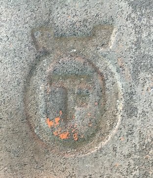 Märkning på betongtakpanna med symbol som liknar "T" eller "F" omgiven av en cirkel.