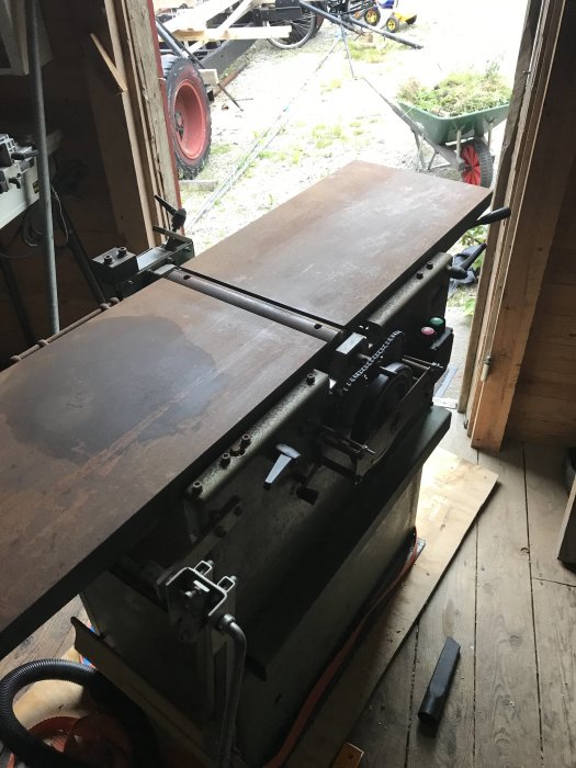 En äldre trähyvelmaskin, Morten RPH 330, utan spånhuv och anhåll, i en verkstadsbod med öppen dörr blickande ut mot en trädgård.