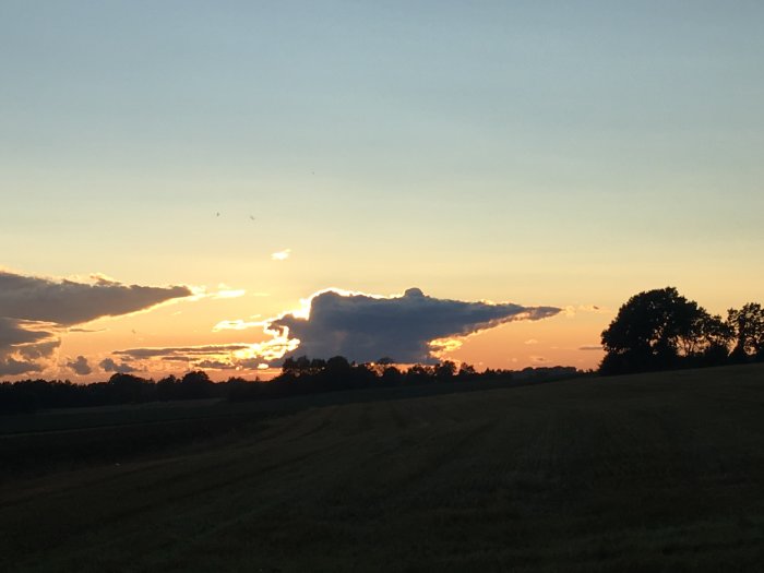 Kvällshimmel efter regn med dramatiska moln och solnedgång över ett fält.