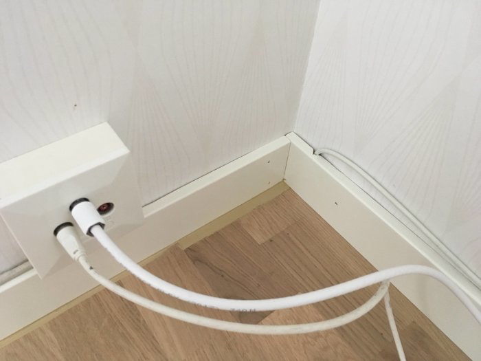 Hörn av rum med ljust trägolv och vit fotlist fogad med Casco S40 och kablar i kabeldosa.