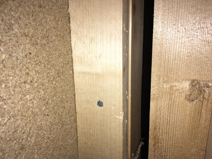 Titthål i vägg visar delen av två träreglar, vilket indikerar väggens konstruktionsdetaljer i en renovering.