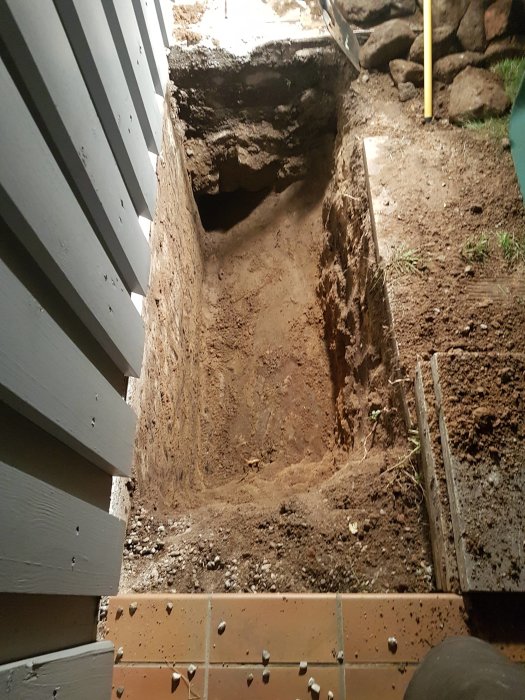 Grävningsarbete i källare med borttagen träpanel och uppgrävd jord.