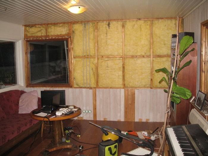 Renoveringsarbete i rum med isolerad vägg utan panel ovanför bröstpanel, fönster och arbetsmaterial syns.