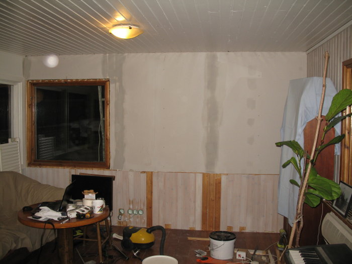 Renoveringsprocess av ett rum där delar av väggar har tagits av för att minska panel, ersatta med gipsskivor under fönster.