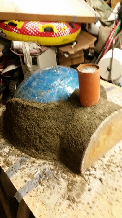 Keskeneräinen vermikuliittibetoni-projekti, johon kuuluu sininen kuntopallo ja oranssi putki puupöydällä autotallissa.